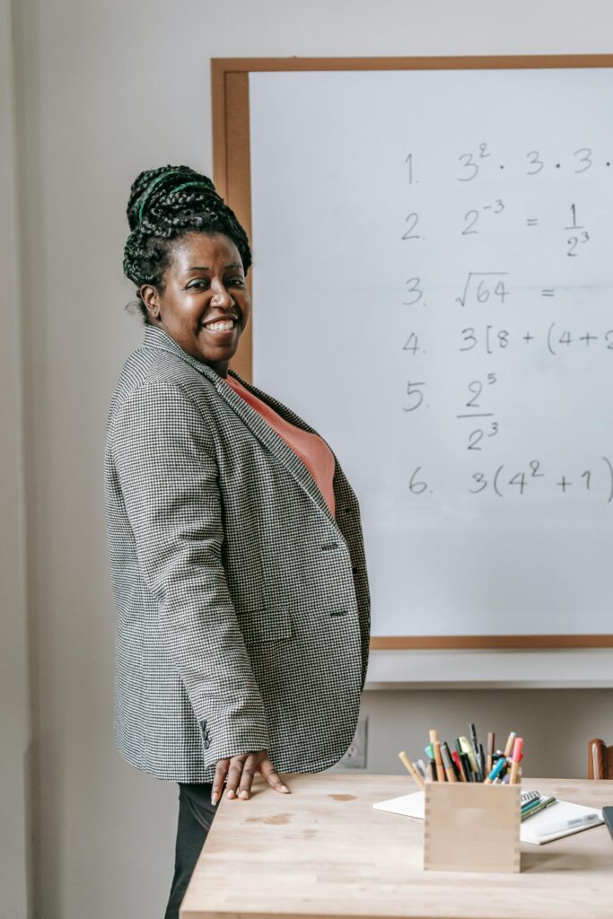 Confident teacher posing by a whiteboard with mathematical equations indoors.